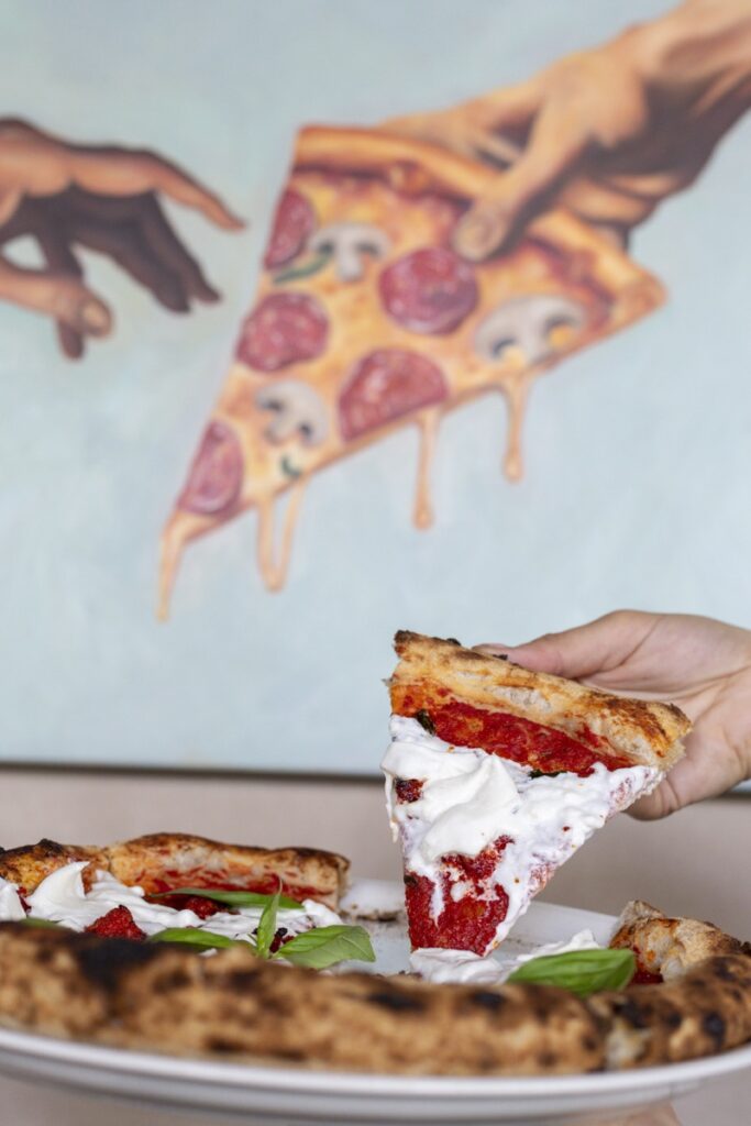 Hand holding woodfired pizza slice with burrata at Bianco Italian Caloundra
