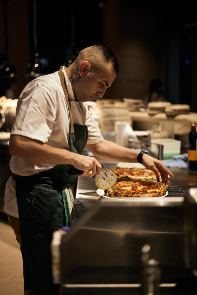 Chef slicing and plating pizza in the kitchen at Bianco Italian restaurant in Caloundra